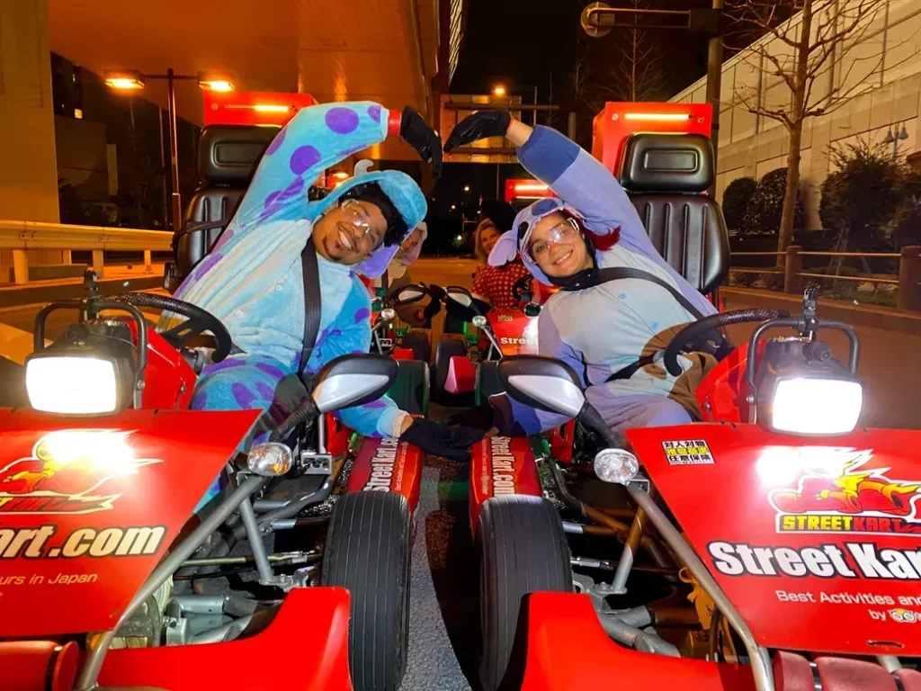 IMG_4272 - StreetKart Two people in blue and purple onesies on red Street Kart go-karts, posing a heart shape with their arms at night on a city street.